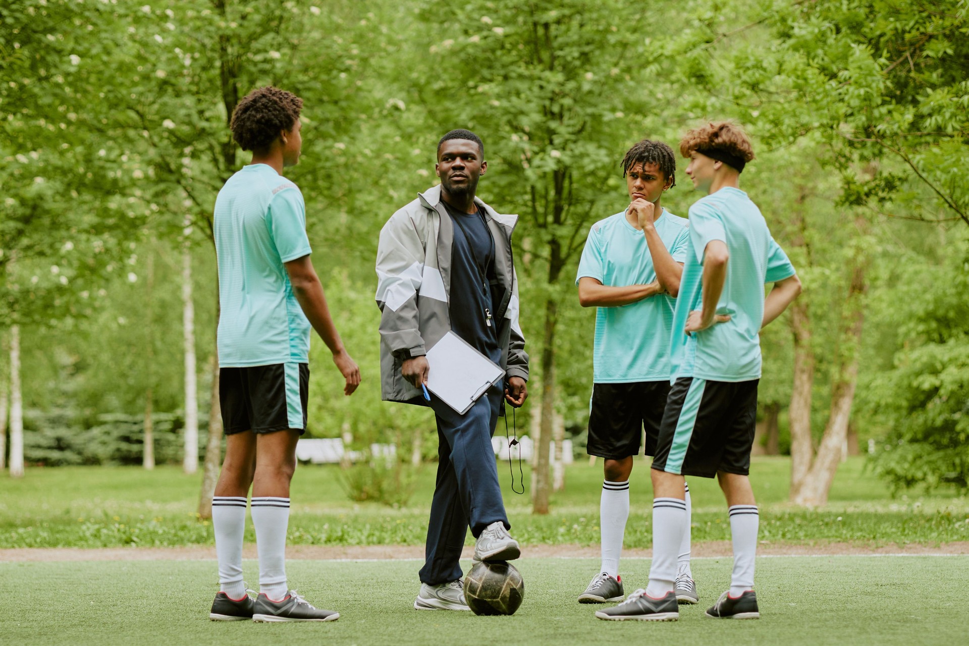 Black Male Coach Instructing Multiethnic Teen Boys during Soccer Practice