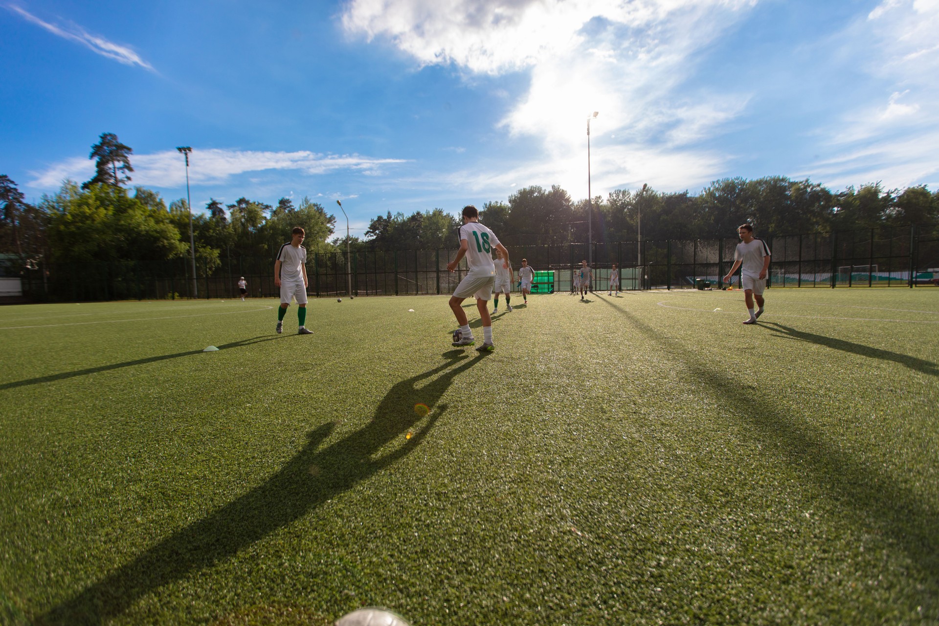 A group of football players training and playing on the field on a sunny day against a blue sky.