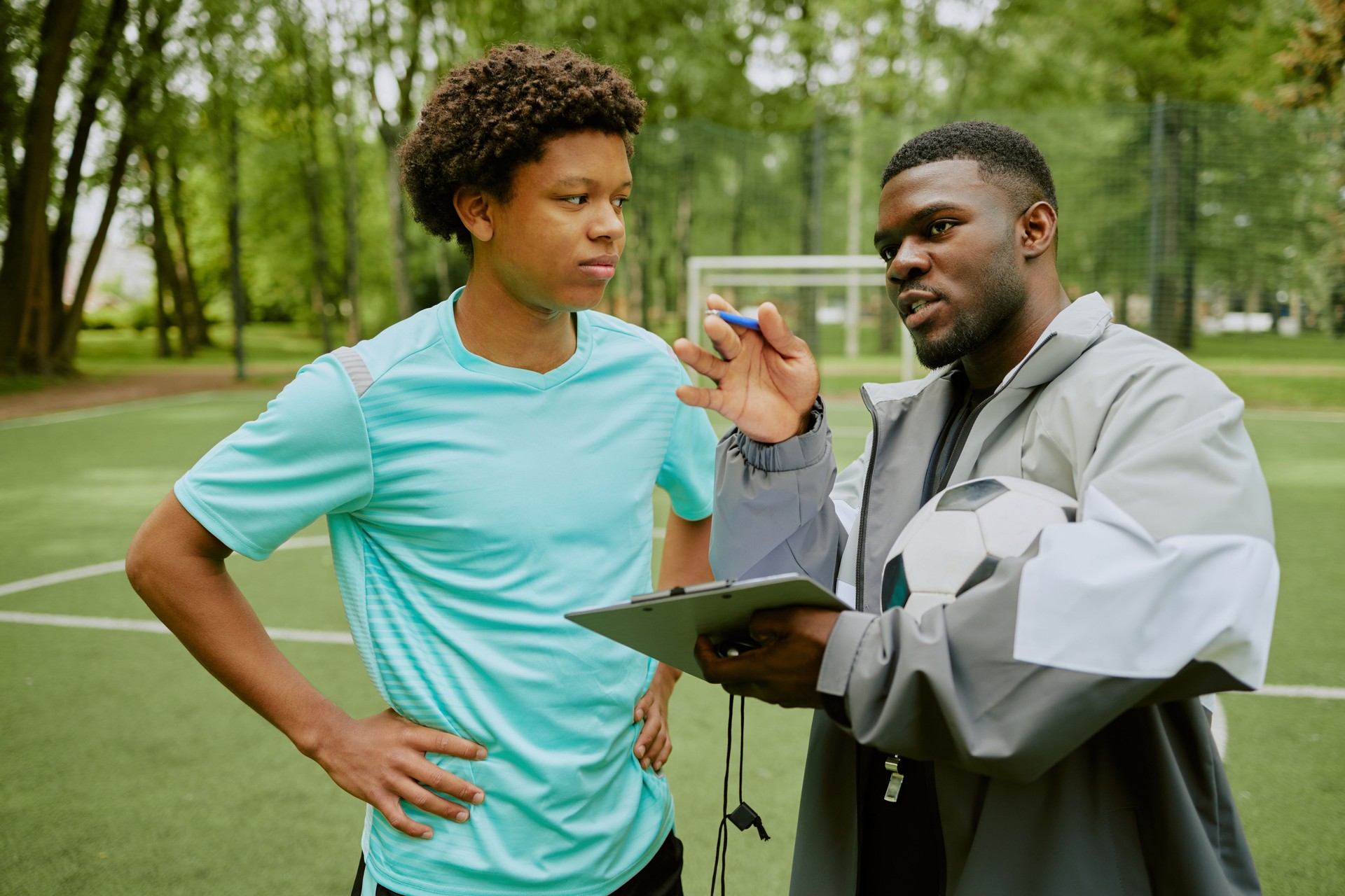 Young Boy Listening to Black Coach Explaining Soccer Strategy Outdoors