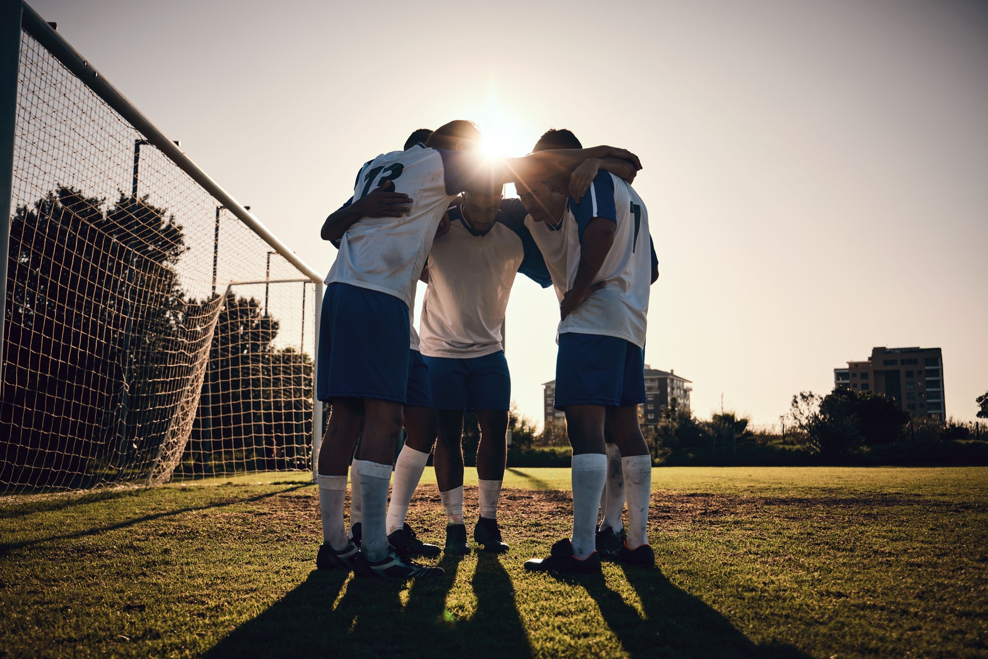 Soccer, sunset or team in a huddle for motivation, goals or group mission on stadium field for a sports game. Match, sunshine or football players planning a strategy, exercise or training for fitness