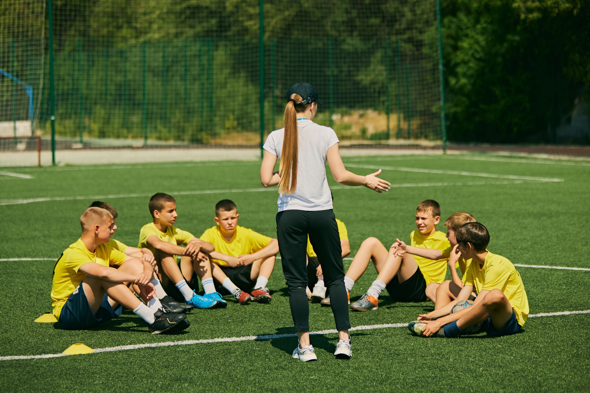 Youth Sports Education. Group of enthusiastic young soccer players listening to strategic advice from female coach, focusing on teamwork and skill development.